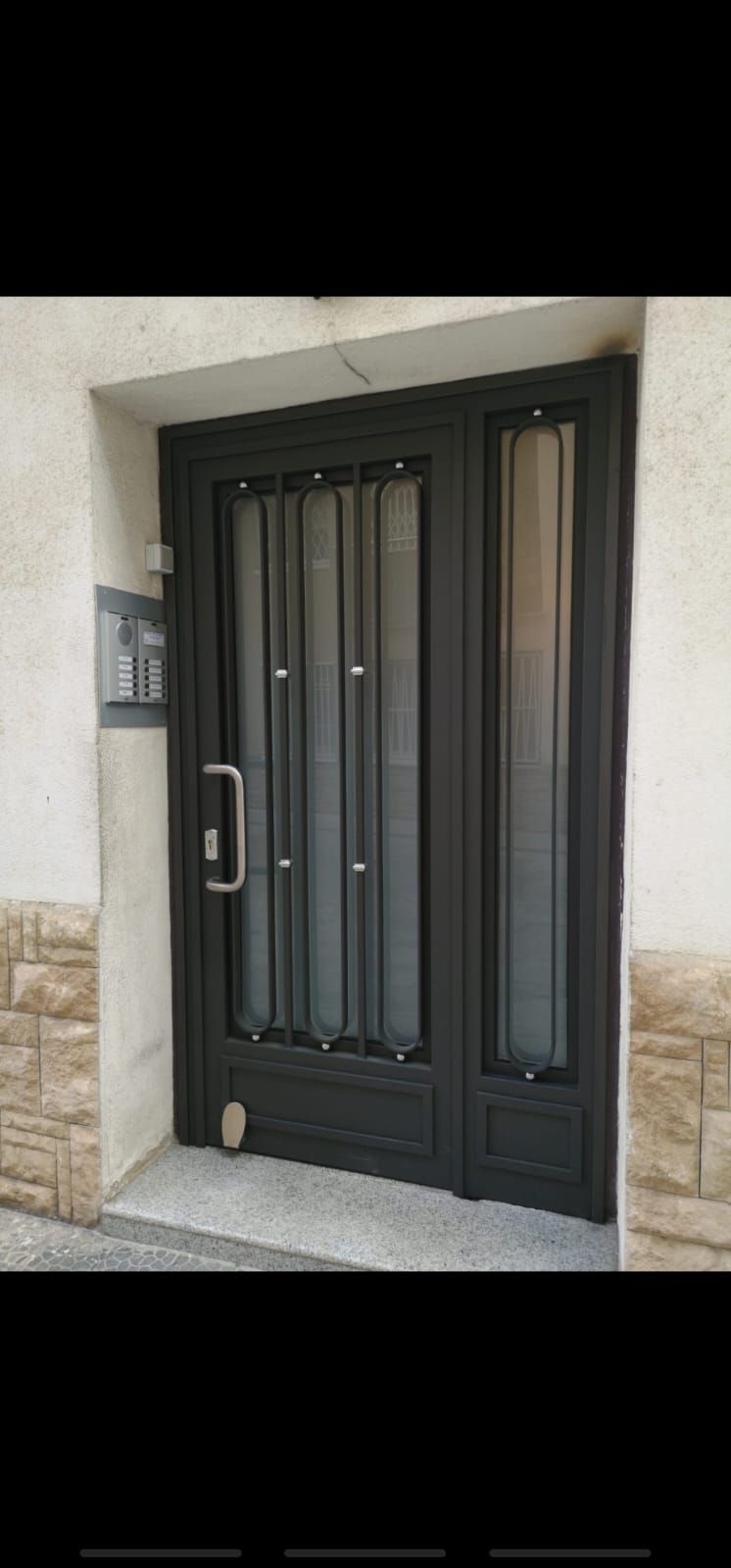 Una puerta negra está sentada al costado de un edificio.