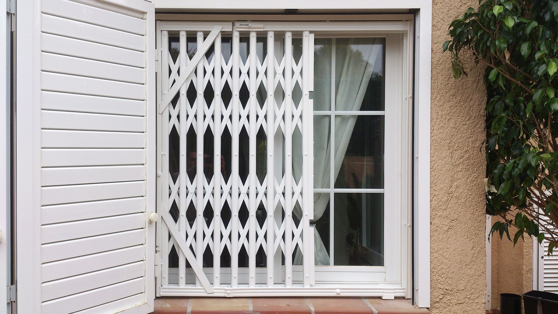 Una ventana con una puerta de metal y contraventanas blancas.