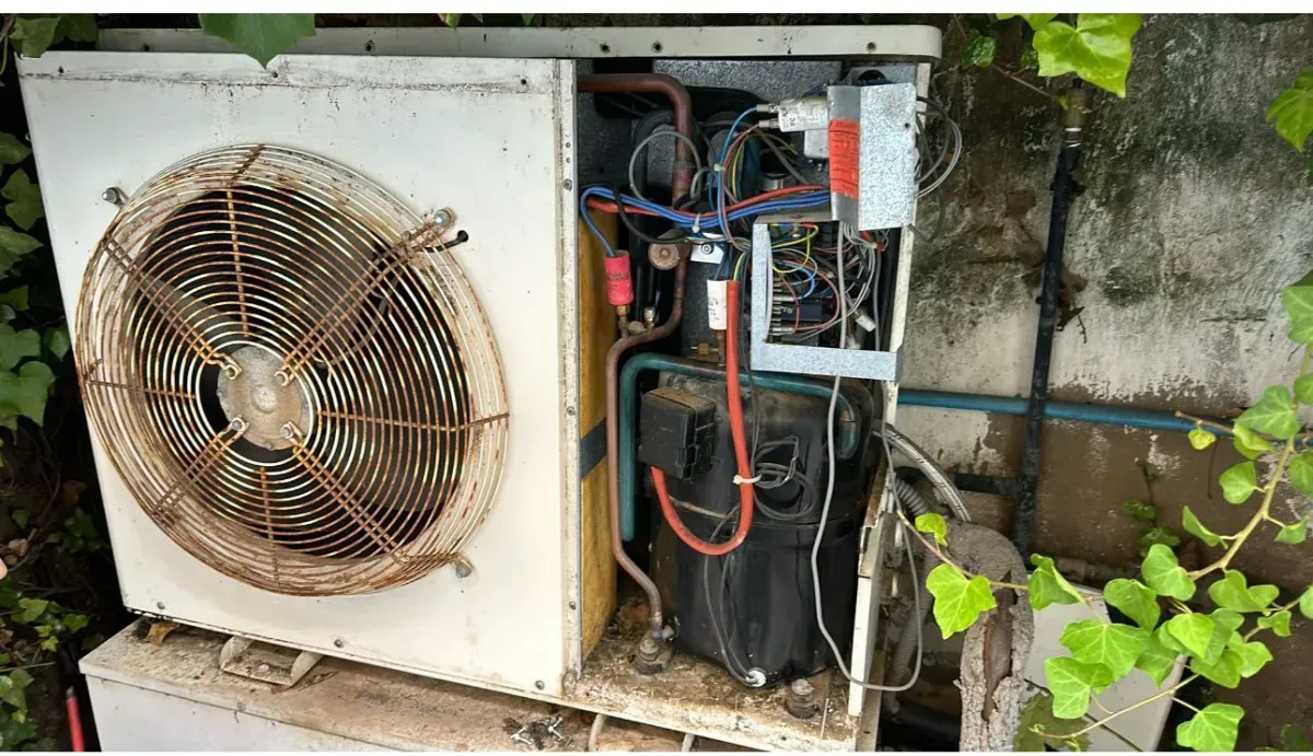 Una unidad exterior de aire acondicionado blanca con el panel lateral retirado, dejando al descubierto el motor interno