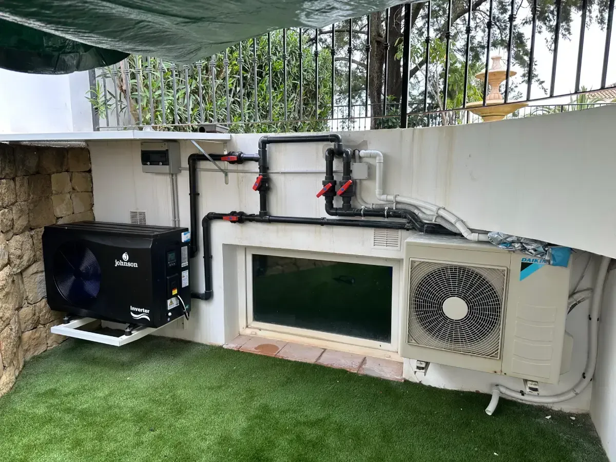 Bomba de calor negra para piscina y unidad de aire acondicionado Daikin blanca montada en una pared exterior con tubería