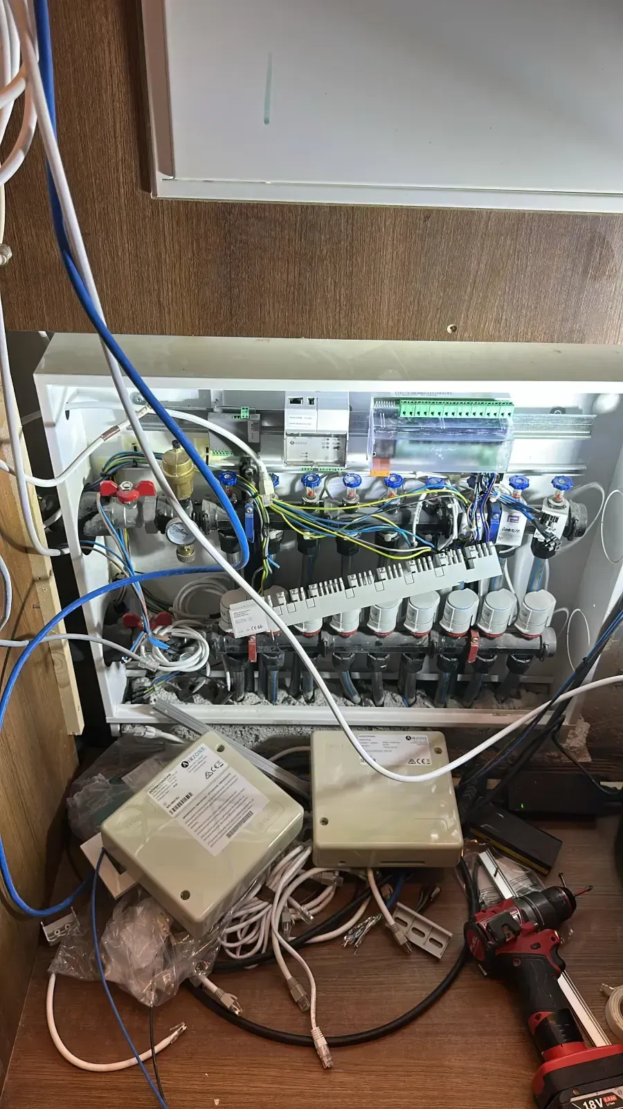 Un colector de control de calefacción parcialmente instalado dentro de un armario de pared, con cableado suelto