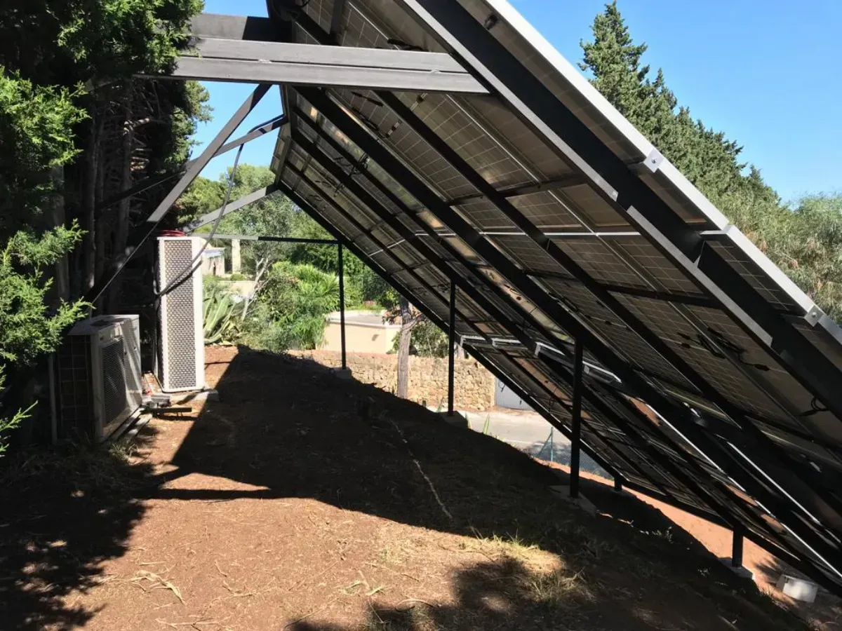 Un conjunto de paneles solares inclinados sobre una estructura metálica, situados en una pendiente de tierra cerca de árboles