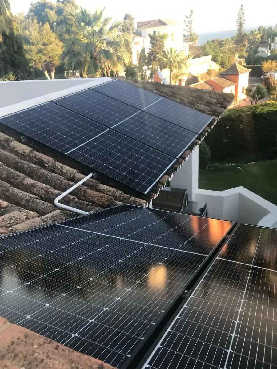 Paneles solares negros instalados en un tejado de tejas con vistas a un jardín paisajístico