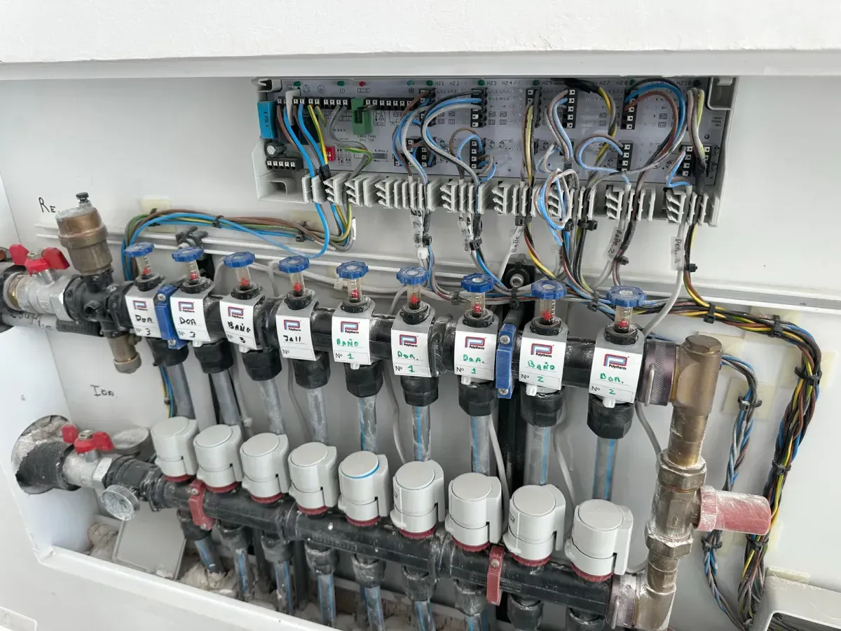 Un colector blanco para calefacción por suelo radiante con cableado eléctrico conectado y una placa de control.