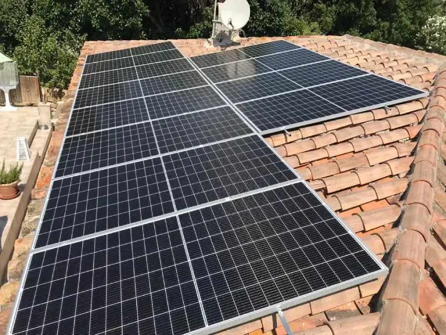 Paneles solares instalados en un tejado de tejas de terracota junto a una antena parabólica.