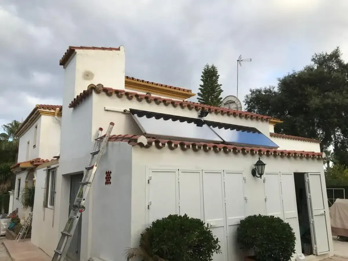 Una casa de estuco blanco con techo de tejas cuenta con paneles solares montados en una sección inclinada del tejado