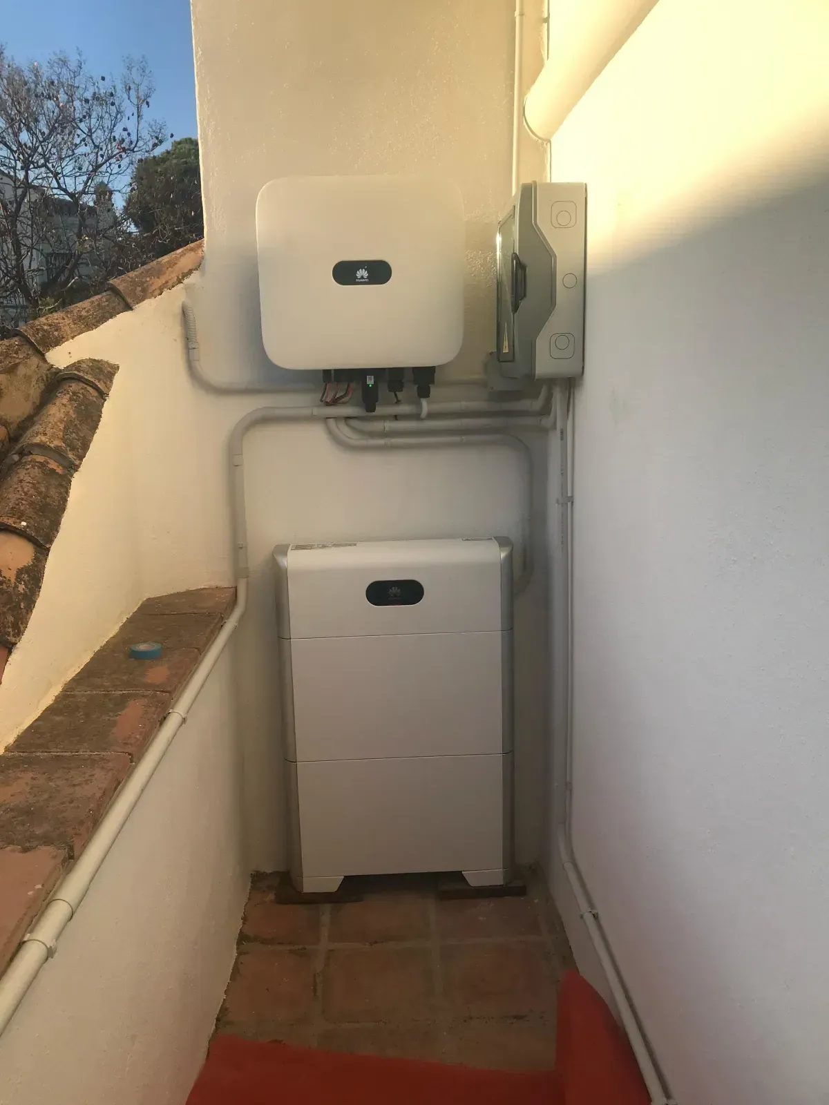 Un inversor solar blanco y una unidad de baterías montados en una pared exterior blanca