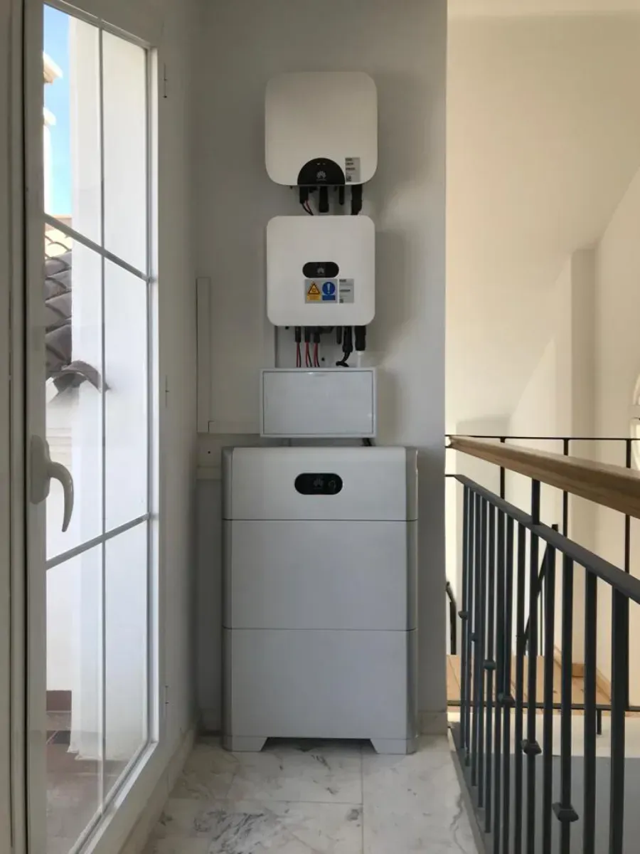 Un sistema de batería e inversor de energía solar de color blanco instalado en una pared junto a la puerta de un balcón