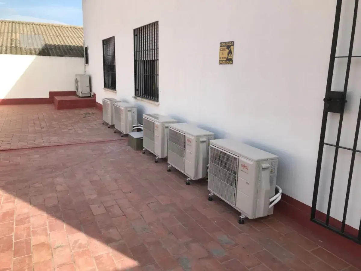 Una hilera de cinco unidades de aire acondicionado exteriores se alineaban contra una pared exterior blanca