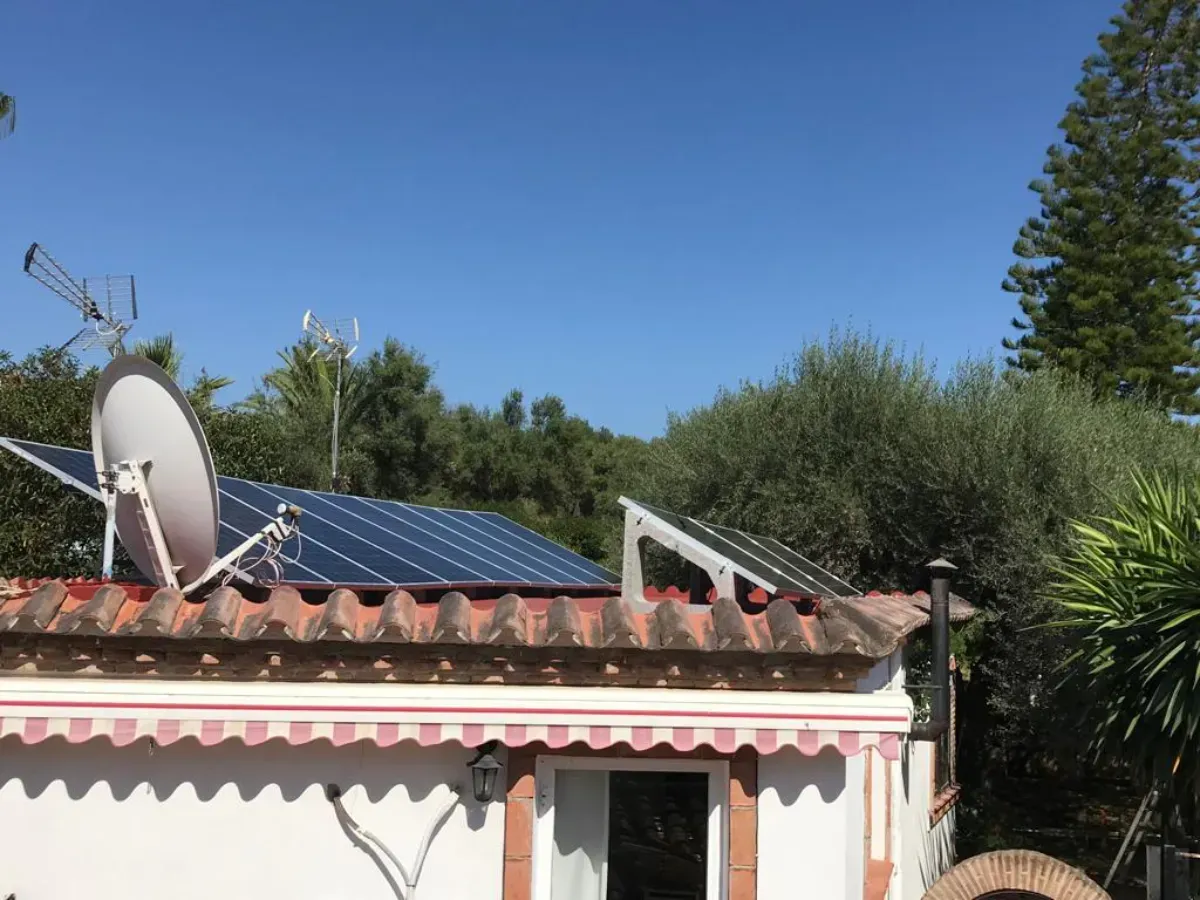 Paneles solares y una antena parabólica instalados en el tejado de tejas de una casa blanca con toldo