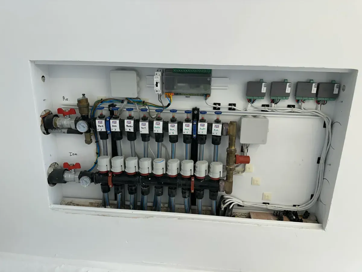 Un armario de servicio de paredes blancas que alberga un colector de calefacción por suelo radiante multizona con tuberías