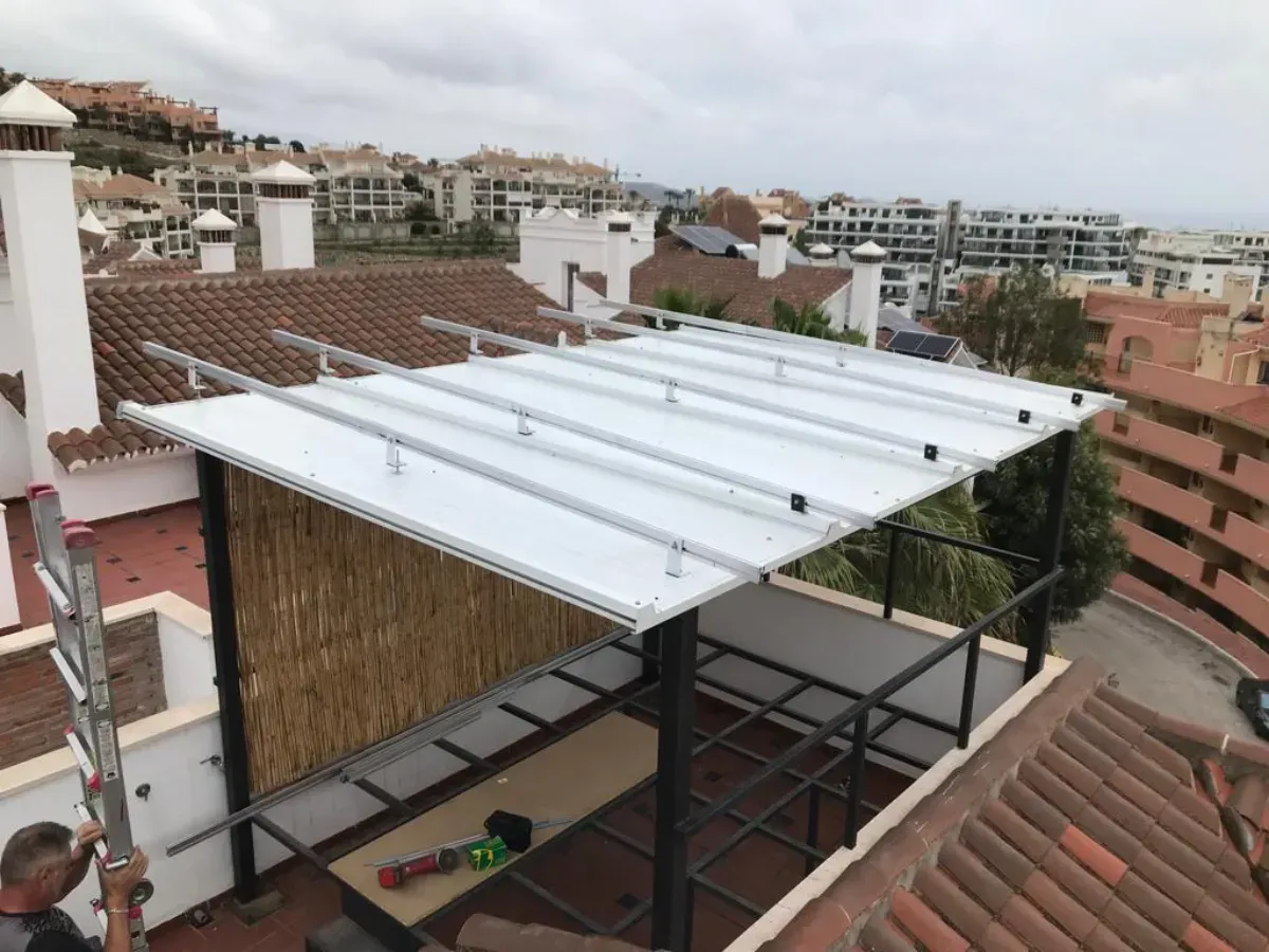 Una persona utiliza una escalera para instalar rieles de montaje para paneles solares en una pérgola de techo plano