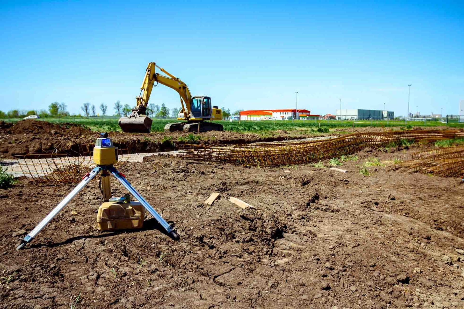 Una obra en construcción con una excavadora al fondo y un trípode en primer plano.