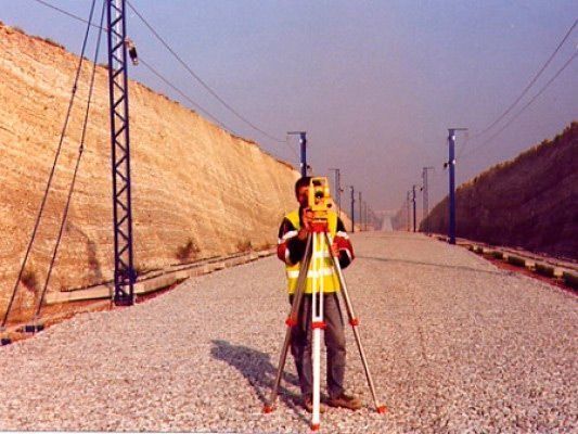 Un hombre está parado en un camino de grava usando un trípode.