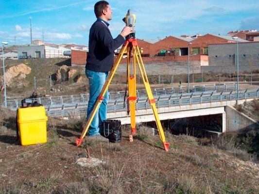 Un hombre está parado en una colina con un trípode frente a un puente.