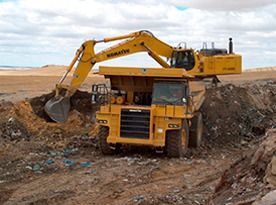 Una excavadora amarilla está cavando un hoyo al lado de un camión volquete.