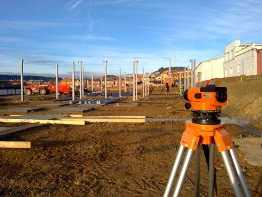 Un nivel naranja está sentado sobre un trípode frente a un edificio en construcción.