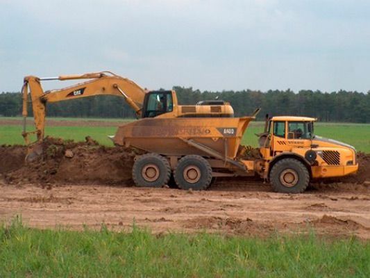 Un camión volquete amarillo está siendo cargado con tierra por una excavadora