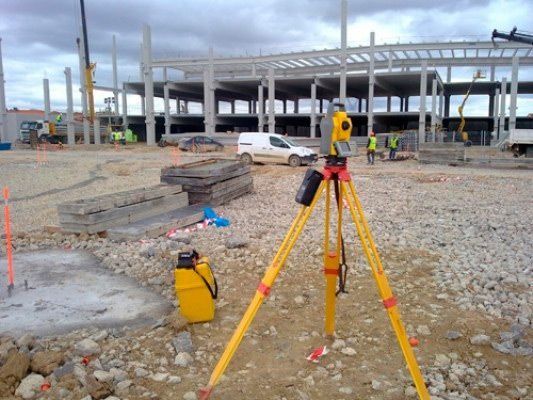 Un trípode está estacionado en el suelo frente a un edificio en construcción.