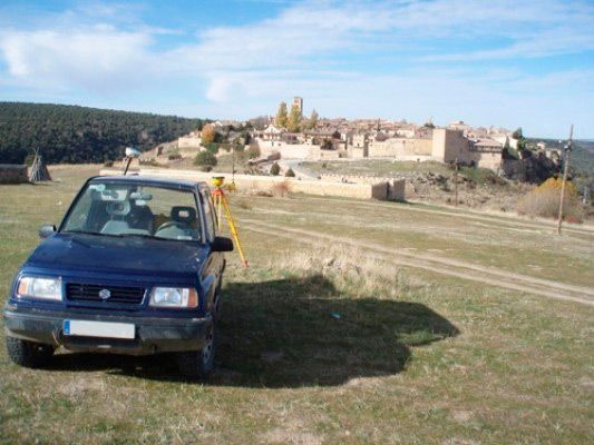 Un coche azul está aparcado en un campo de hierba con un castillo al fondo.