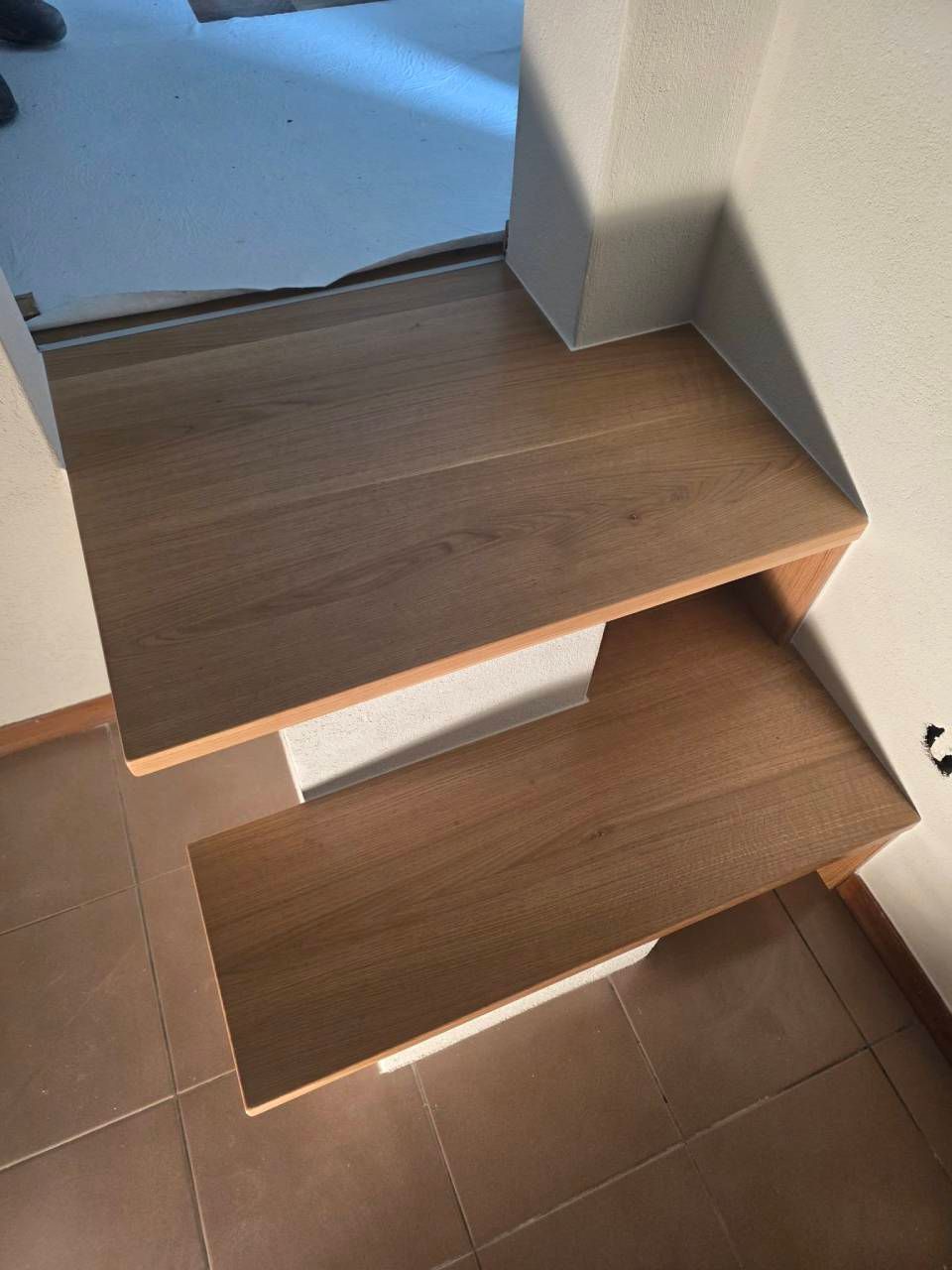 Scala moderna in legno con pianerottolo in un corridoio interno piastrellato.