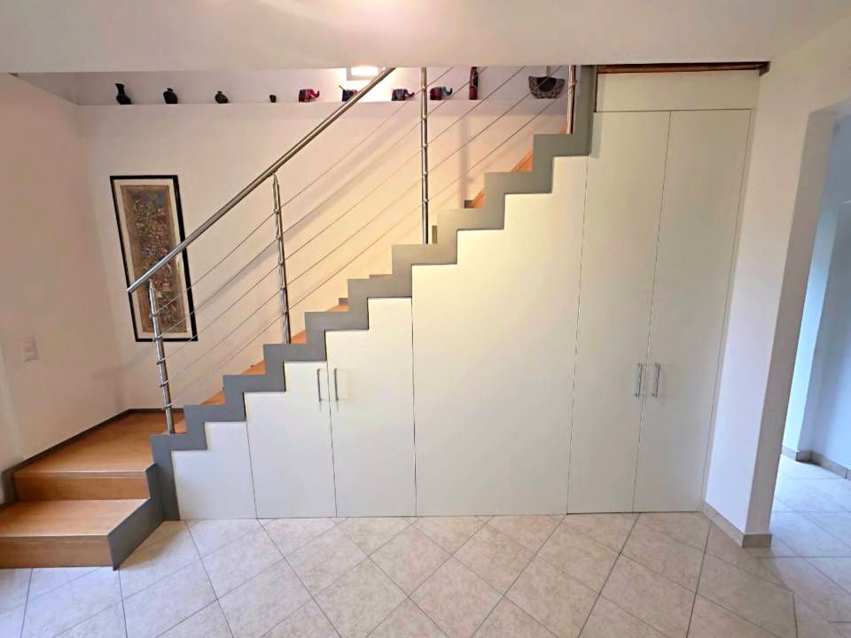 Scala interna con pareti bianche, pavimento piastrellato e ripostiglio integrato sotto le scale.