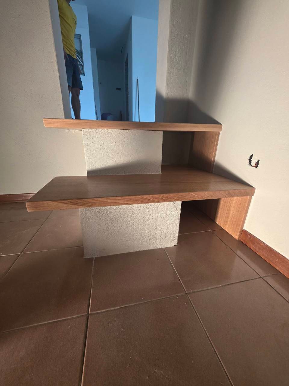 Scala in legno con due gradini sospesi e un supporto centrale bianco in un corridoio piastrellato.