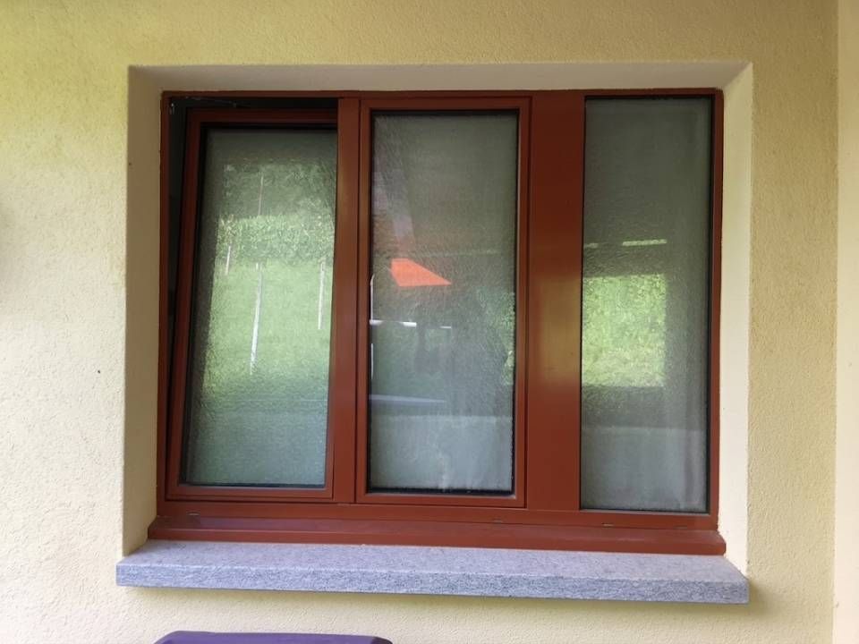 Finestra con cornice marrone e vetro satinato incastonata in una parete beige.