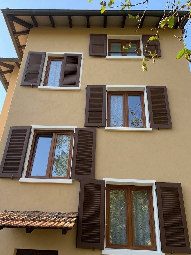 Facciata beige dell'edificio con numerose finestre e persiane marroni che si stagliano contro un cielo limpido.