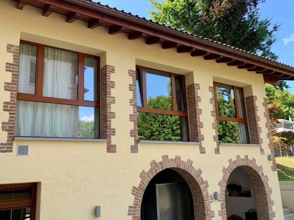 Facciata della casa color crema con finestre incorniciate di marrone e due portali ad arco sotto un tetto di tegole.
