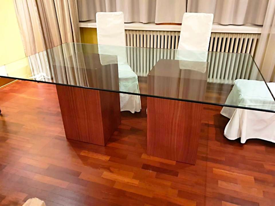 Un tavolo da pranzo in vetro con due sedie bianche su un pavimento in legno in una stanza luminosa.