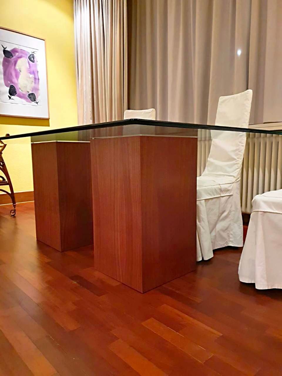 Un tavolo da conferenza in legno in una sala riunioni con sedie rivestite di bianco e tende beige.