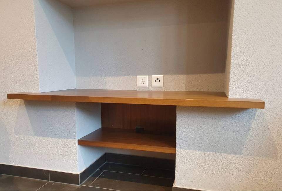 Angolo scrivania in legno integrato con mensole e prese a muro in una stanza minimalista