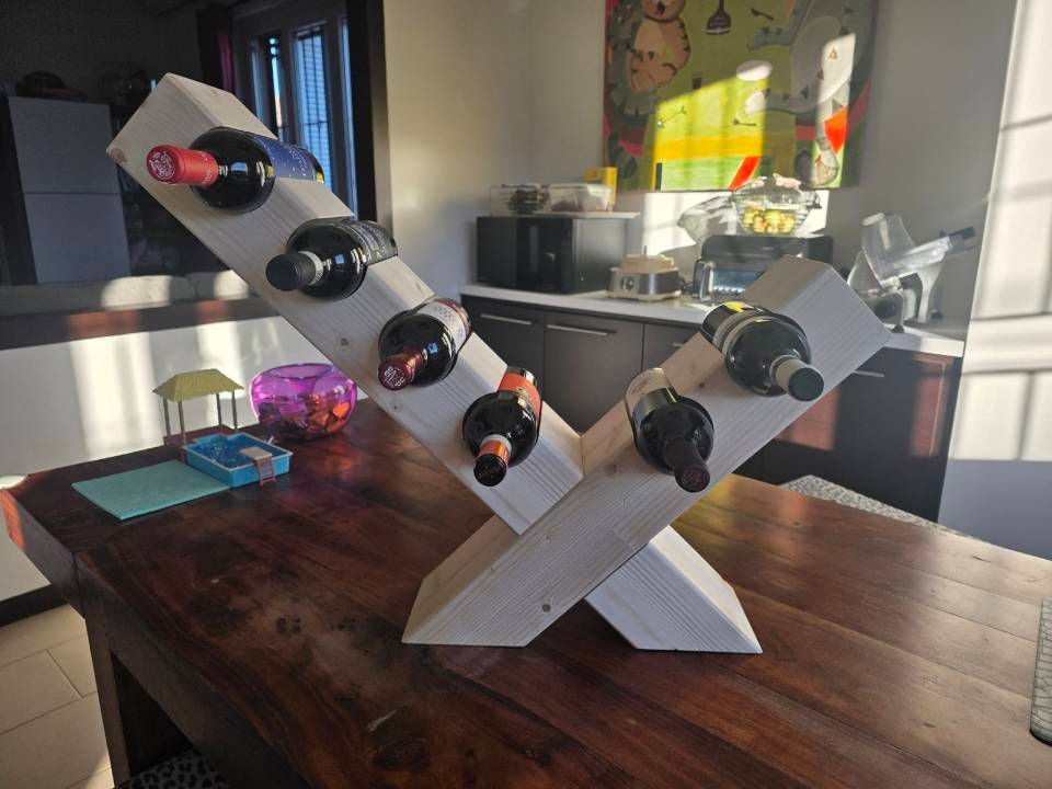 Portabottiglie geometrico bianco con bottiglie nere su un tavolo di legno in una cucina illuminata dal sole.