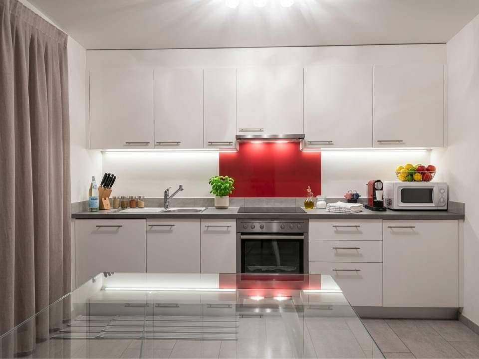 Cucina moderna bianca con paraschizzi rosso, forno a incasso, ripiani e grande tenda sulla sinistra.