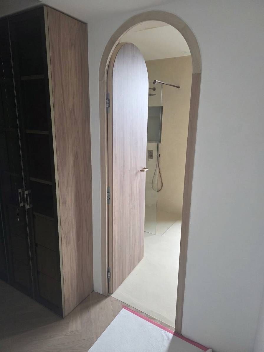 Porta ad arco in un corridoio che conduce a un bagno luminoso, con pavimento piastrellato e pareti chiare.