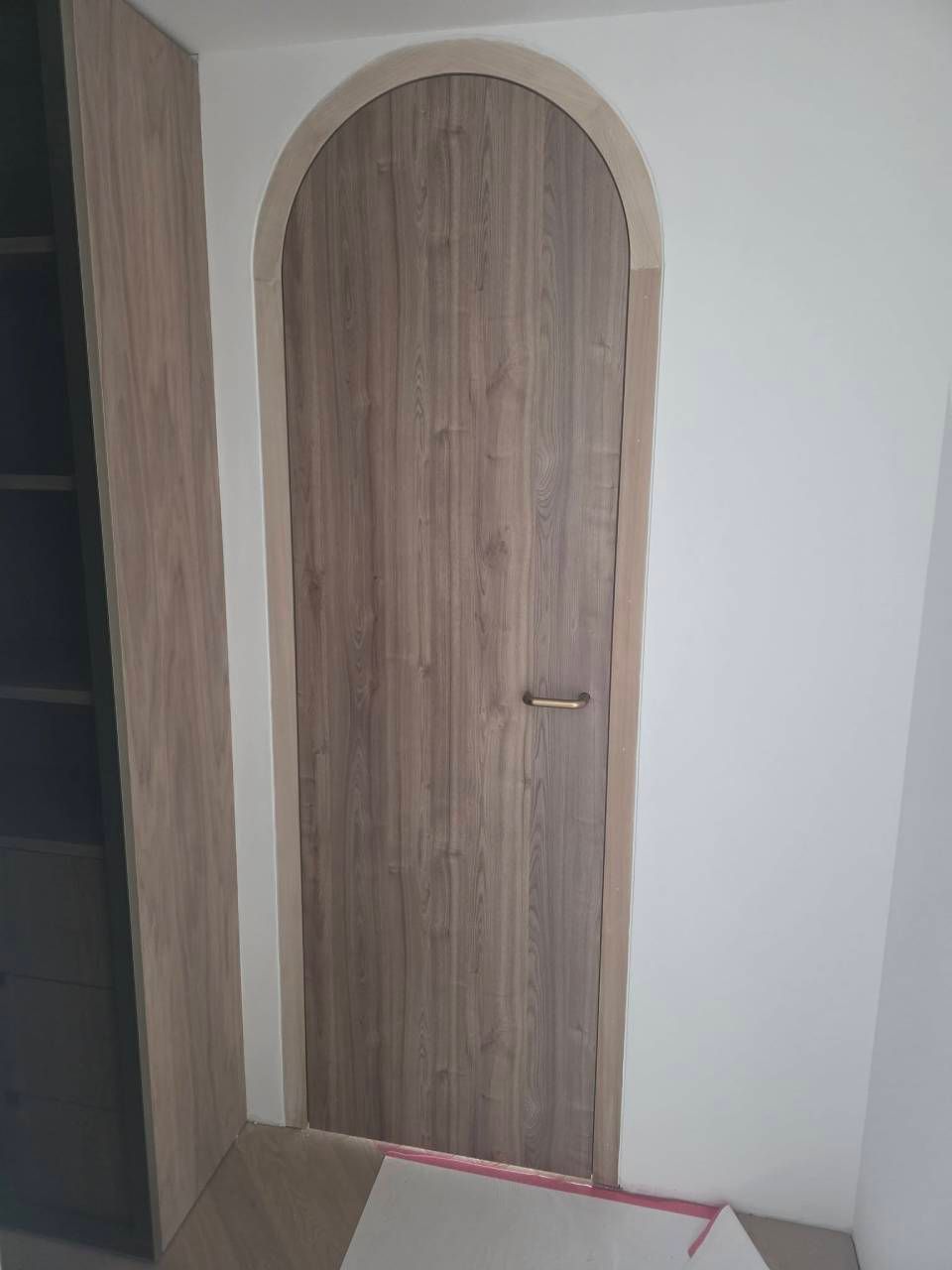 Porta di legno ad arco in un corridoio bianco, con una scatola di cartone in primo piano.