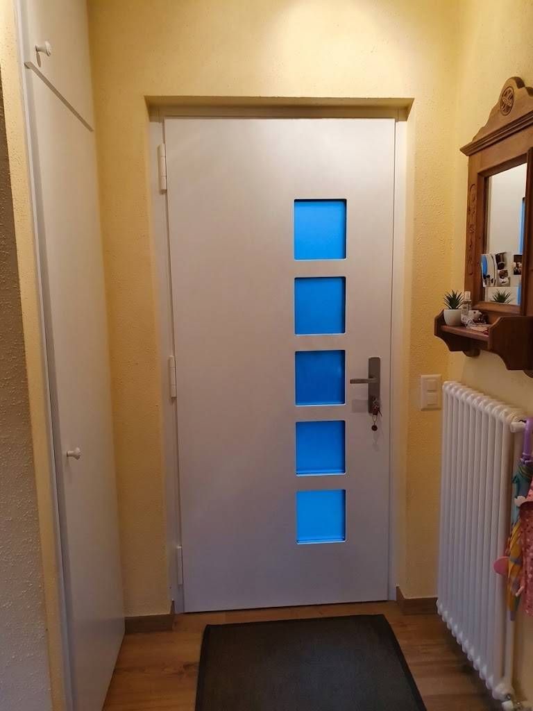 Corridoio con porta d'ingresso bianca, pannelli in vetro blu, zerbino scuro e termosifone sulla destra.