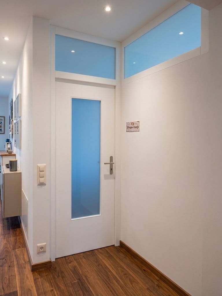 Corridoio bianco con porta dotata di pannelli in vetro satinato e pavimento in legno.
