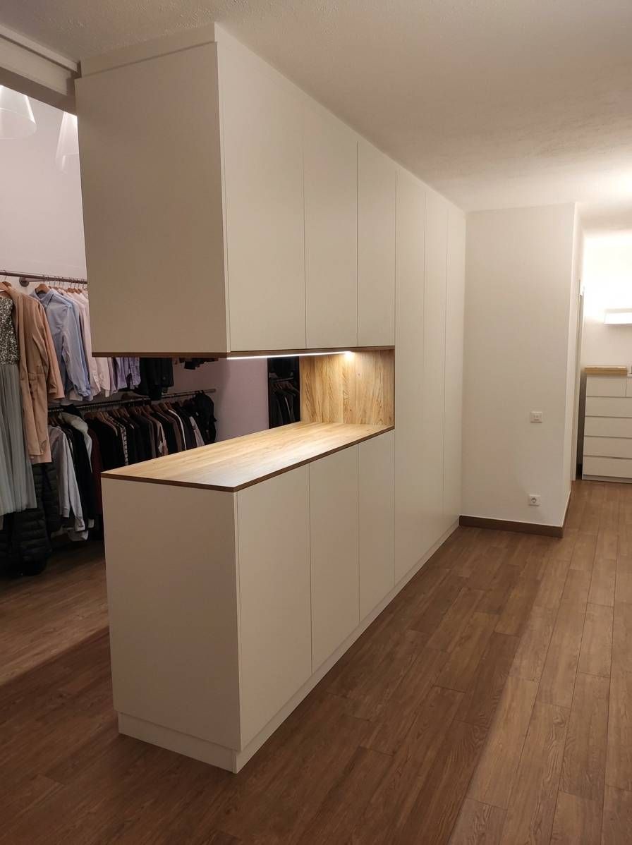 Stretto corridoio con armadi a muro bianchi, una mensola passavivande illuminata, pavimento in legno e armadio per i vestiti sulla sinistra.