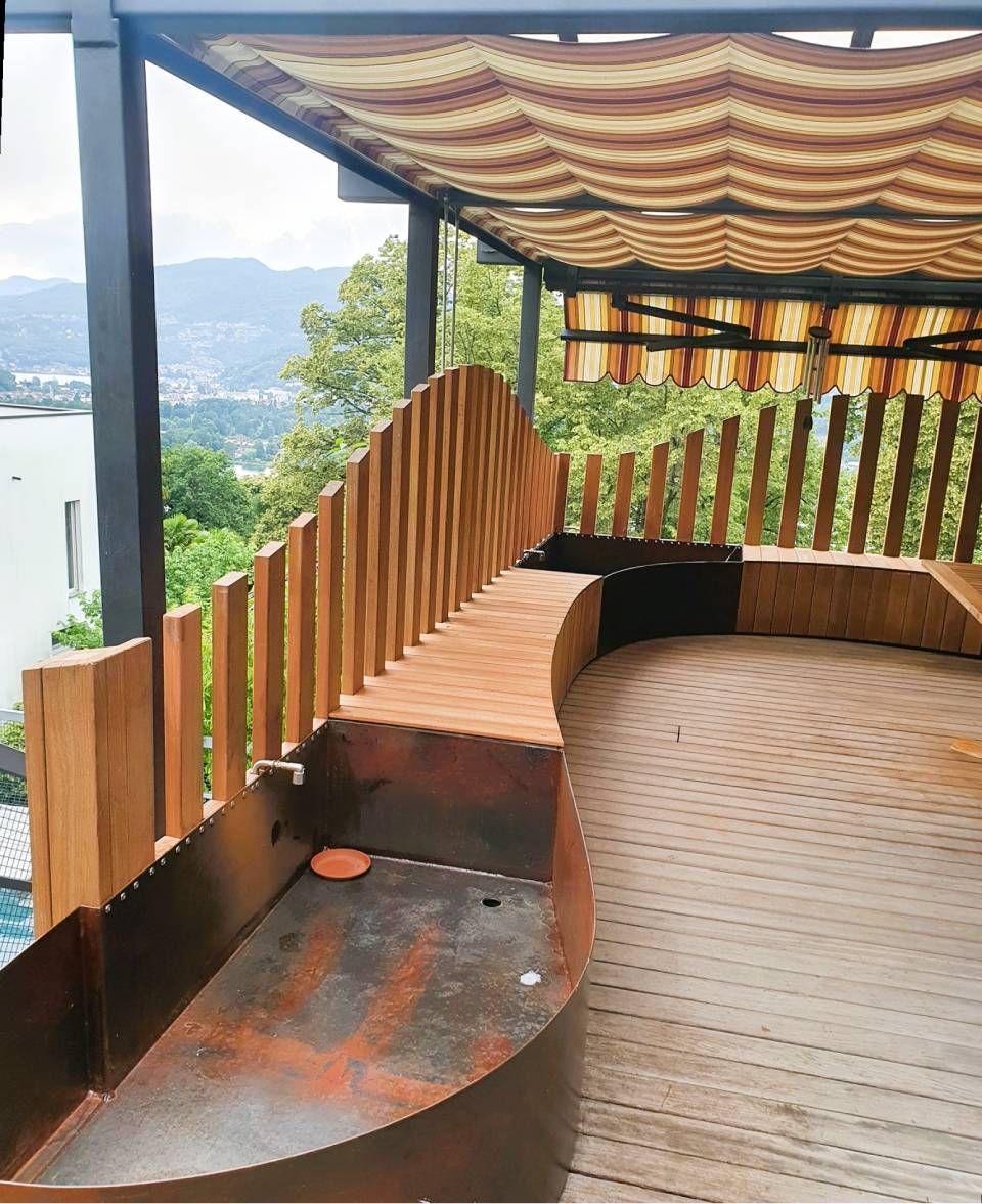 Terrazza curva in legno con tettoia a strisce e vista sulle montagne oltre la ringhiera.