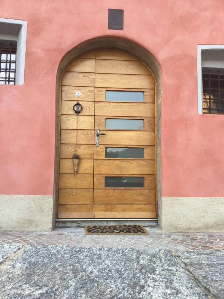 Porta ad arco in legno in una parete di stucco rosa con piccole finestre e soglia in ciottoli.