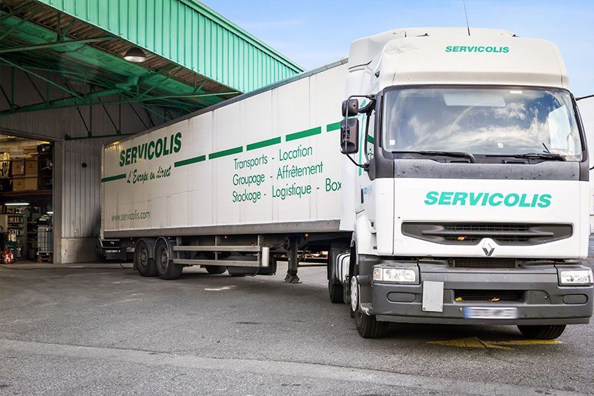 Camion blanc Servicolis à quai de chargement, texte et logo verts, jour.