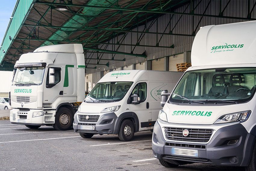 Trois véhicules de livraison Servicolis stationnés sous un auvent de quai de chargement.