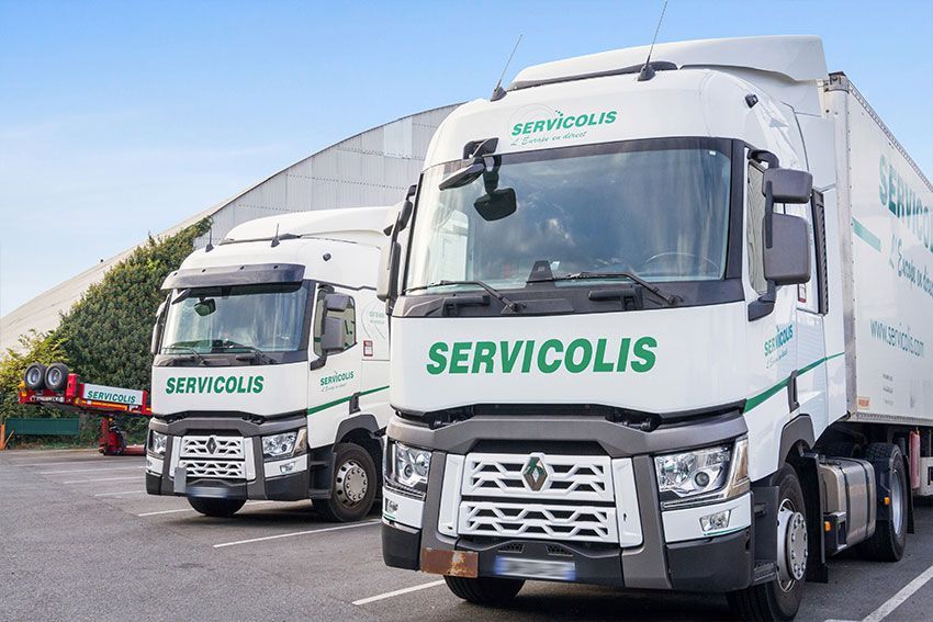 Deux camions blancs Servicolis stationnés devant un entrepôt.