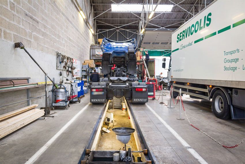 Camion dans un atelier de réparation avec une remorque Servicolis. Vidange d'huile et outils visibles.