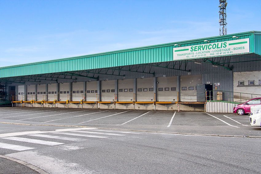 Entrepôt avec quais de chargement, auvent vert, parking et enseigne SERVILICOLIS.