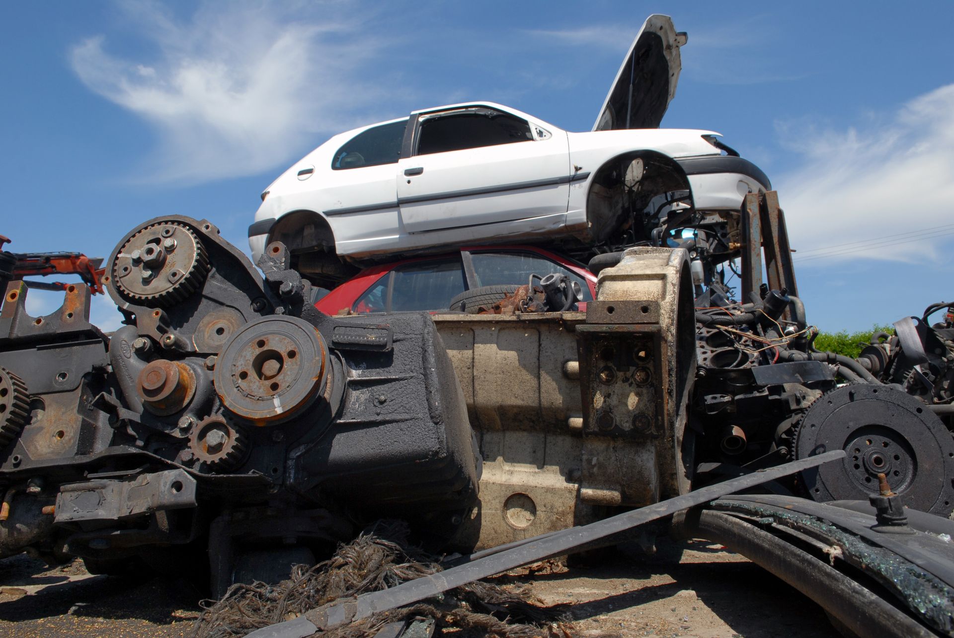 Casse automobile : une voiture blanche sur des pièces de moteur, d'autres composants automobiles empilés.