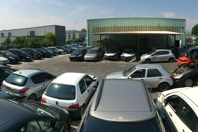 Voitures garées dans une casse, certaines sous un toit en tôle ondulée.