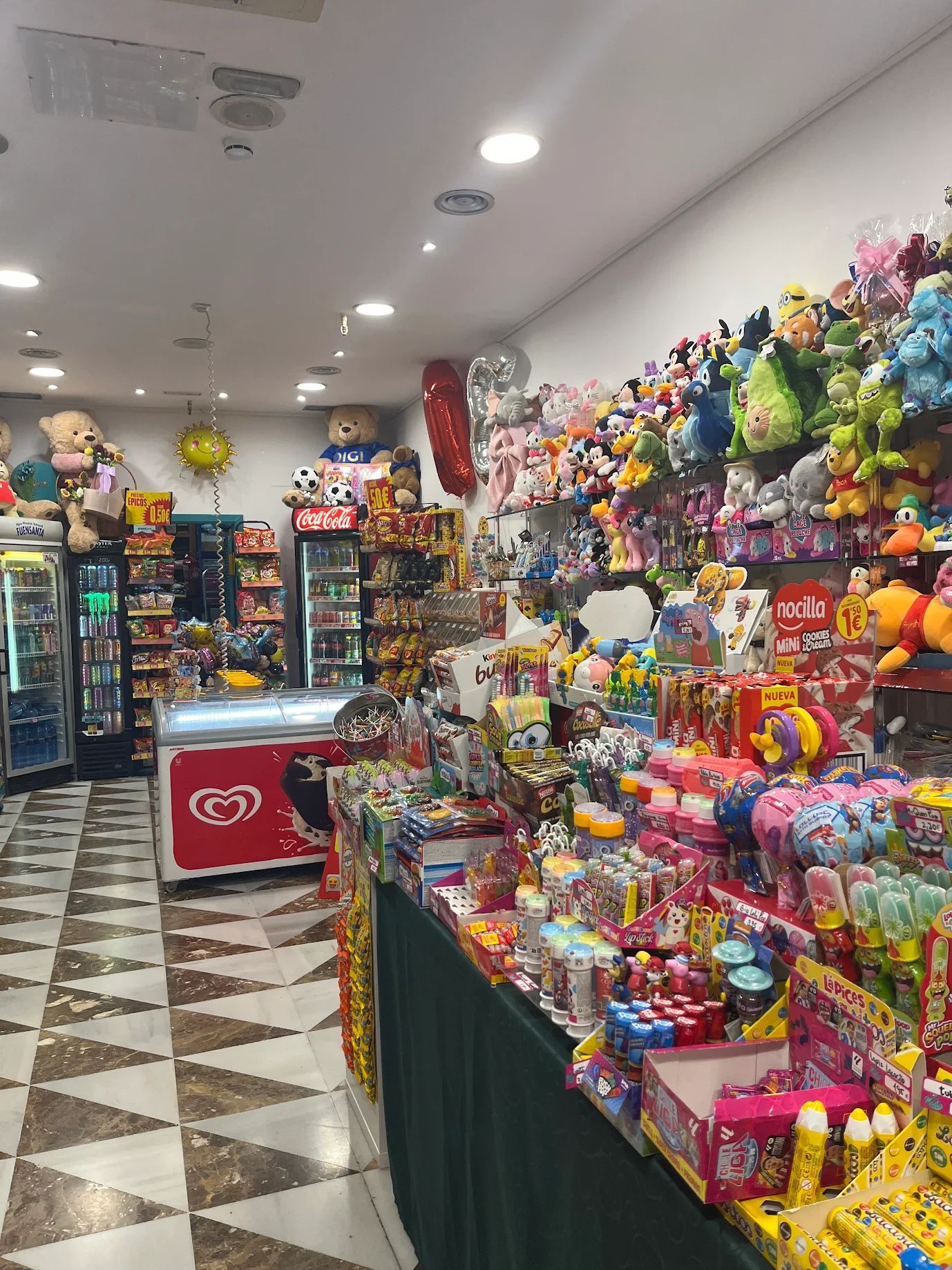 Dentro de una colorida tienda de juguetes y dulces, llena de peluches y golosinas.